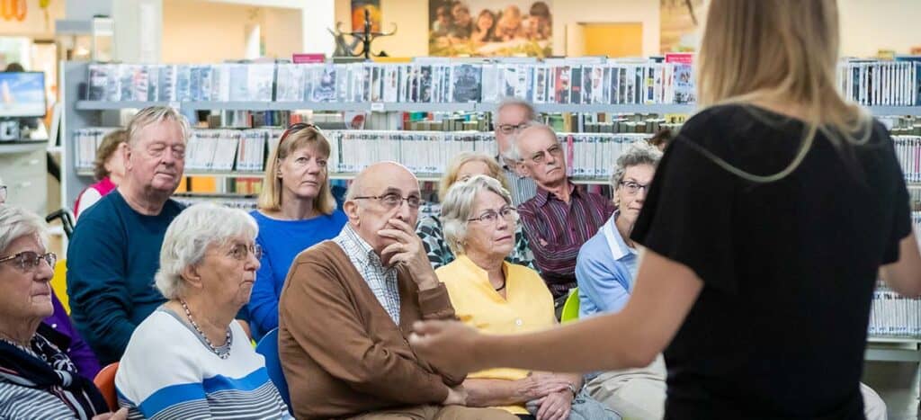 Deelnemers volgen een seniorencollege van een studentdocent in een bibliotheek